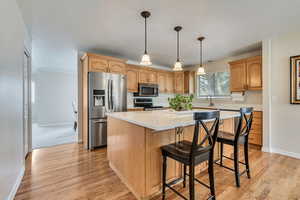 Kitchen featuring stainless steel appliances, a kitchen island, light wood-type flooring, a breakfast bar area, and light countertops