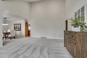 Living room with light carpet, baseboards, a towering ceiling, crown molding, and plenty of natural light