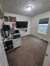 Home office with a textured ceiling, dark colored carpet, and baseboards