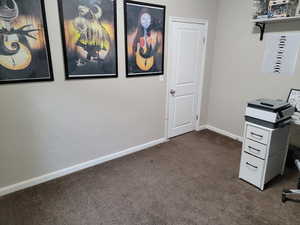 Unfurnished office featuring dark colored carpet, baseboards, and a textured wall