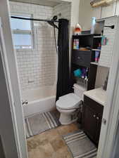Bathroom featuring vanity, toilet, shower / tub combo with curtain, and a textured wall