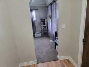 Hall with a textured wall, arched walkways, wood finished floors, ornamental molding, and baseboards