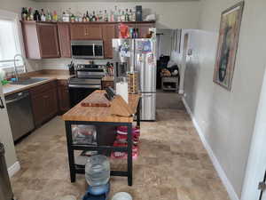 Kitchen featuring appliances with stainless steel finishes, a sink, stone finish flooring, and baseboards