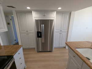 Kitchen featuring stainless steel fridge, light wood-style floors, recessed lighting, stone countertops, and white cabinetry