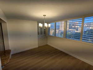 Unfurnished dining area featuring baseboards, a chandelier, and dark wood finished floors