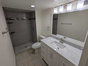 Full bathroom featuring toilet, tiled shower, vanity, marble finish flooring, and recessed lighting