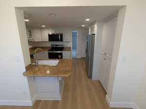 Kitchen featuring stainless steel appliances, a sink, a peninsula, light stone counters, and light wood-type flooring