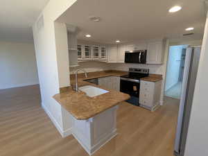 Kitchen featuring appliances with stainless steel finishes, a peninsula, light wood finished floors, white cabinetry, and a sink