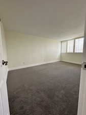 Spare room featuring dark carpet and baseboards