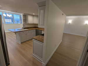 Kitchen with baseboards, open shelves, appliances with stainless steel finishes, a sink, and light wood-style floors