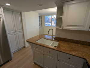Kitchen featuring freestanding refrigerator, a sink, light wood-type flooring, recessed lighting, and white cabinetry