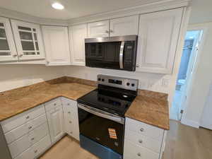 Kitchen featuring stainless steel microwave, electric range, light wood finished floors, white cabinets, and recessed lighting