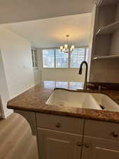 Kitchen with a sink, dark stone countertops, a chandelier, baseboards, and open shelves