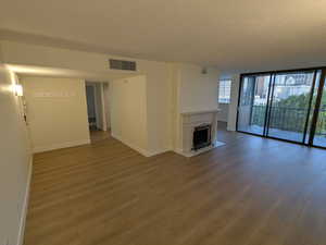 Unfurnished living room featuring baseboards, wood fstyle finished floors, floor to ceiling windows, and a fireplace