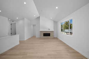 Unfurnished living room featuring recessed lighting, vaulted ceiling, a tiled fireplace, light wood finished floors, and baseboards