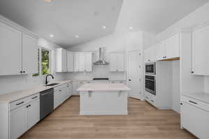Kitchen with stainless steel appliances, wall chimney exhaust hood, a sink, a center island, and white cabinets