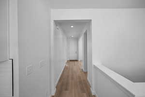 Corridor with light wood-style floors, recessed lighting, baseboards, and an upstairs landing