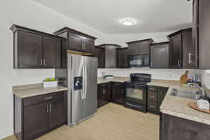 Kitchen with black appliances, a sink, light wood-style flooring, dark brown cabinets, and light countertops
