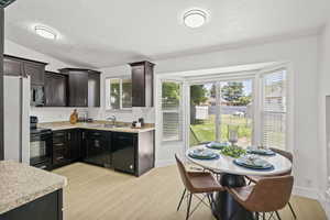 Kitchen with black appliances, a textured ceiling, a sink, light countertops, and light wood-style flooring