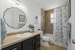 Bathroom featuring toilet, shower / bathtub combination with curtain, vanity, and wood finished floors