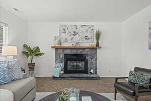 Carpeted living room with a stone fireplace and baseboards
