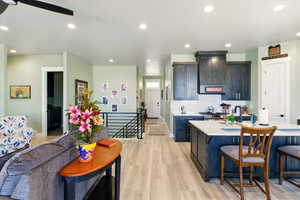 Kitchen with light countertops, a breakfast bar, light wood-type flooring, wall chimney exhaust hood, and recessed lighting