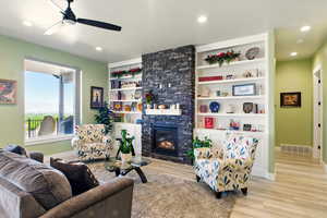 Living area with a ceiling fan, baseboards, wood finished floors, a stone fireplace, and recessed lighting