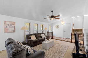 Carpeted living area with stairs, vaulted ceiling, ceiling fan, a chandelier, and tile patterned floors