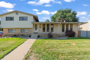 Tri-level home with brick siding, a porch, and a front lawn