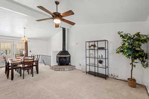 Carpeted dining room with a wood stove, vaulted ceiling, and ceiling fan