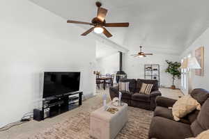 Living room featuring carpet, a wood stove, lofted ceiling, and a ceiling fan