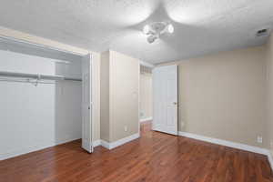 Unfurnished bedroom featuring dark wood-style flooring, a textured ceiling, and a closet