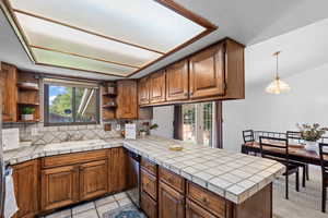 Kitchen featuring brown cabinetry, a peninsula, backsplash, dishwasher, and light tile patterned floors