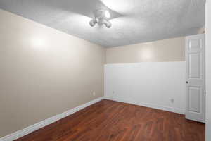 Empty room featuring a textured ceiling and dark wood-style flooring
