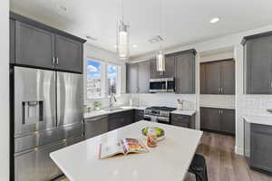 Kitchen featuring appliances with stainless steel finishes, a sink, light countertops, backsplash, and dark wood-style floors