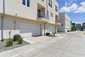 View of property featuring central air condition unit, a residential view, an attached garage, and concrete driveway