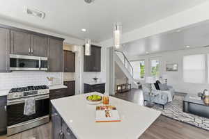 Kitchen featuring stainless steel appliances, light countertops, wood finished floors, dark brown cabinetry, and decorative backsplash