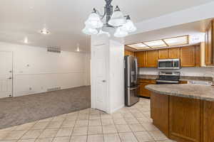 Kitchen with light tile patterned floors, light carpet, brown cabinetry, dark countertops, and pendant lighting