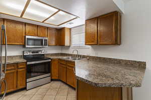 Kitchen featuring brown cabinetry, appliances with stainless steel finishes, and light tile patterned floors
