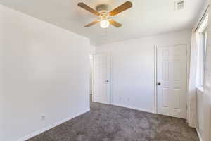 Unfurnished bedroom with dark carpet and a ceiling fan