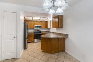 Kitchen with brown cabinets, a peninsula, appliances with stainless steel finishes, and light tile patterned floors