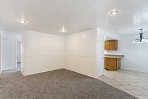 Empty room featuring light carpet, light tile patterned flooring, and a chandelier