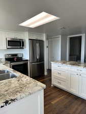 Kitchen featuring stainless steel appliances, white cabinets, dark wood-style flooring, and light stone counters