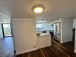 Kitchen with appliances with stainless steel finishes, a peninsula, dark wood-type flooring, light stone counters, and a textured ceiling
