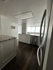Kitchen featuring stainless steel appliances, dark wood-type flooring, a sink, light stone counters, and a textured ceiling