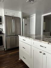 Kitchen featuring appliances with stainless steel finishes, dark wood-type flooring, white cabinets, light stone counters, and a textured ceiling