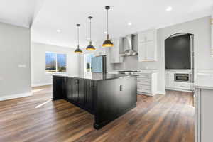 Kitchen featuring wall chimney exhaust hood, smart refrigerator, wood finished floors, arched walkways, and baseboards