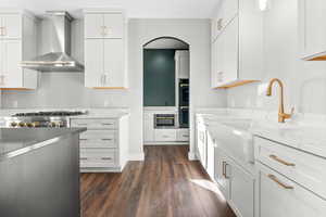 Kitchen featuring wall chimney range hood, dark wood finished floors, a sink, and white cabinets