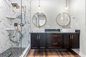 Bathroom featuring double vanity, a marble finish shower, wood finished floors, and baseboards