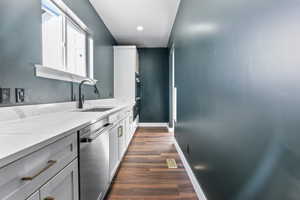 Kitchen with dishwasher, light stone counters, a sink, dark wood-type flooring, and baseboards